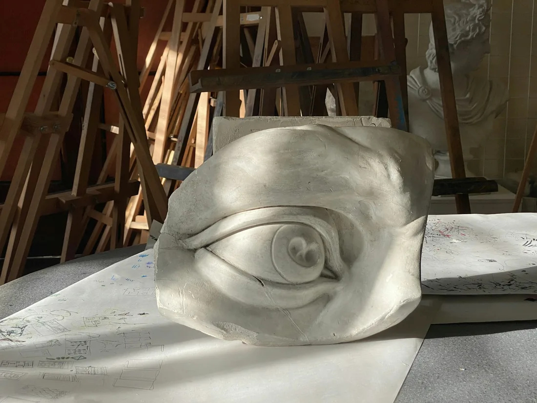 Vaciado en escayola de un ojo de gran tamaño sobre una mesa de taller, con caballetes y moldes al fondo